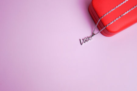 Silver pendant in shape of inscription love on red box. Pink background. Valentines Day, birthday, March 8th. Giftの写真素材