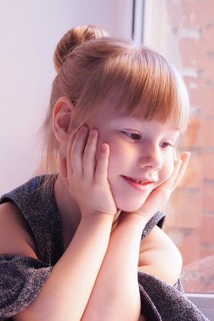 Beautiful little girl with high hairstyle looks out windows.