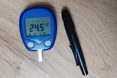 A blood glucose meter with a high blood sugar reading lies on a wooden table. Blood sugar measurements. The concept of diabetes. Hypoglycemia. Copy space.の写真素材