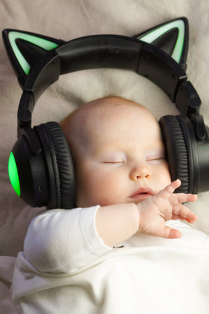 The infant sleeps in black earbuds in the shape of cat ears on a white bed.の写真素材