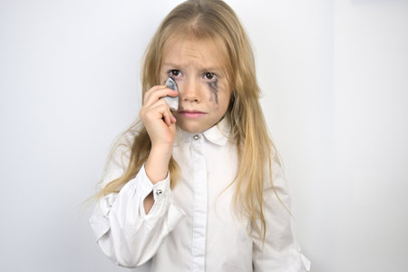 A little girl with brown disheveled hair on a white background. Leaky mascara, tears, anxiety, stress.の写真素材