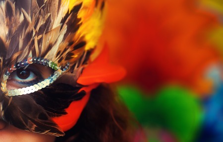 Young woman with a colorful feather carnival face mask on bright colorful background, eye contact, make up artistの写真素材