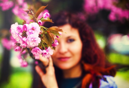 Young woman smelling a beautiful sakura blossom, pink flowers.の写真素材