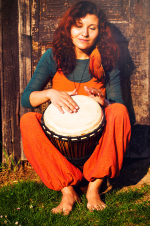 Young barefoot lady drummer playing on her djembe drum on rustic wooden door background.の写真素材