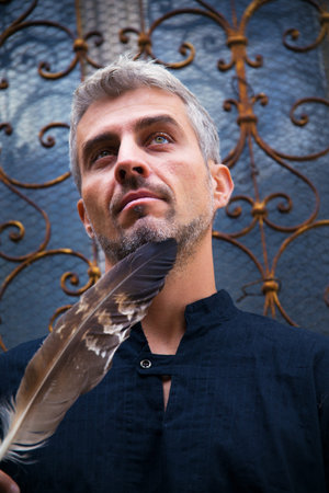 Portrait of a sexy man and eagle feathers, and ornamental medieval window on background.の写真素材