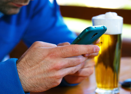 Closeup of male hands with  smart phone and  beer background.の写真素材