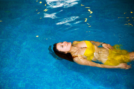 portrait of a young woman relaxing in a swimming pool. swim in the pool  and yellow swimsuit. Copy space.の写真素材