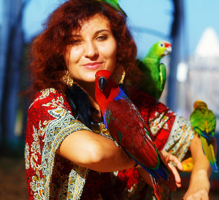 Young woman in ornamental dress and beautiful gold jewelry with a color parrots.の写真素材