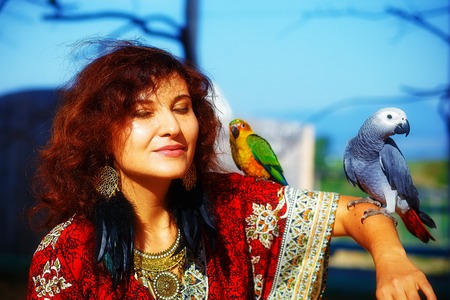 Young woman in ornamental dress and beautiful gold jewelry with a color parrots.の写真素材