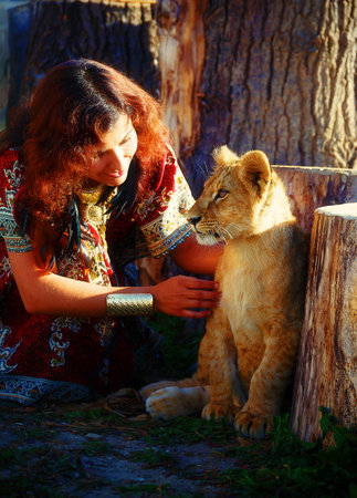 young woman with ornamental dress and gold jewel playing with lion cub in natureの写真素材