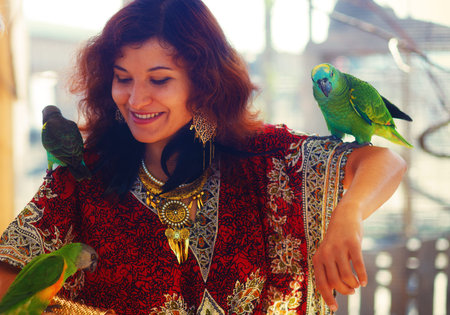 Young woman in ornamental dress and beautiful gold jewelry with a color parrots.