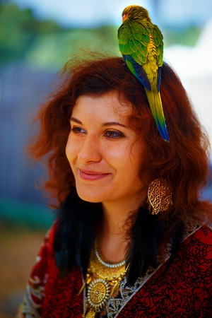 Young woman in ornamental dress and beautiful gold jewelry with a color parrots in hairの写真素材