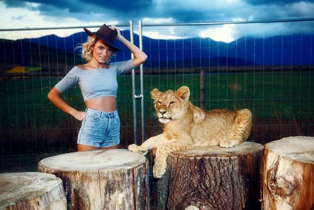 sexy woman  in a western hat with lion cub on background with beautiful sky and storm clouds.の写真素材