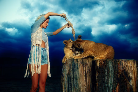 sexy blonde woman playing with lion cub on background with beautiful blue sky and storm cloudsの写真素材