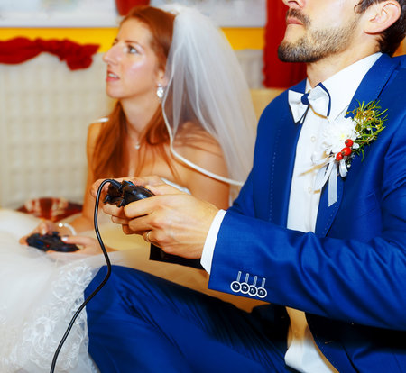 bride and groom playing together videogames with joysticks - gaming and wedding concept
