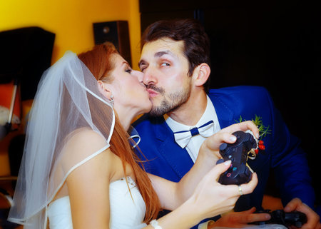 bride and groom playing together videogames with joysticks - gaming and wedding concept