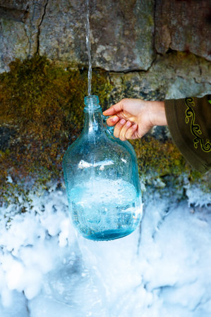 Woman hand with bottle at a beautiful frozen winter spring