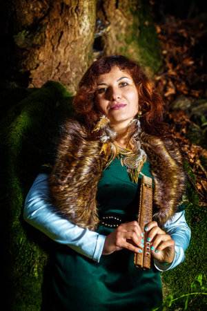 girl in historic dress with wooden flute in woodland country with bemoosed rocks.の写真素材