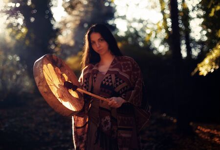 beautiful shamanic girl playing on shaman frame drum in the nature.の写真素材