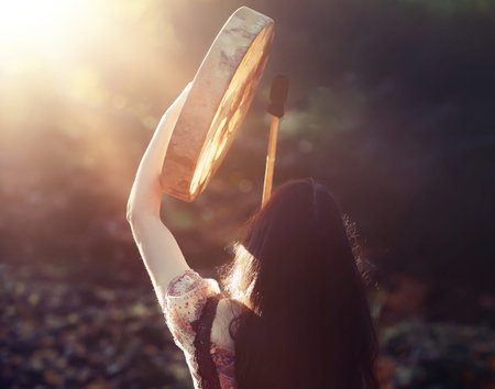 beautiful shamanic girl playing on shaman frame drum in the nature.の写真素材
