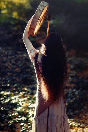 beautiful shamanic girl playing on shaman frame drum in the nature.の写真素材