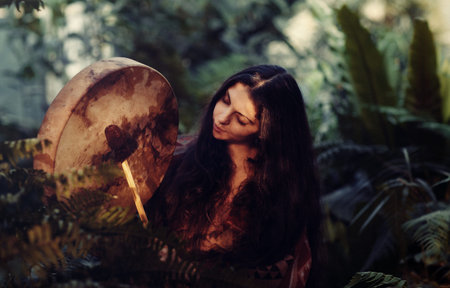 beautiful shamanic girl playing on shaman frame drum in the sunlight.