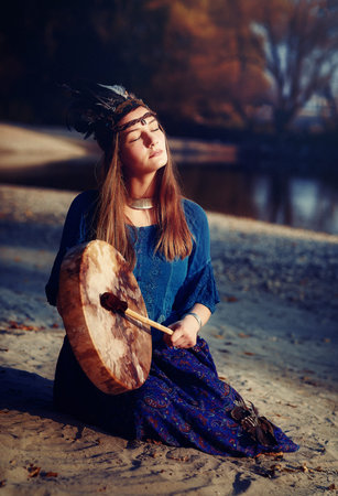 beautiful shamanic girl playing on shaman frame drum in the nature.