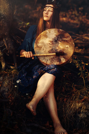 beautiful shamanic girl playing on shaman frame drum in the nature.