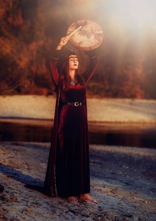 beautiful shamanic girl playing on shaman frame drum in the nature.の写真素材