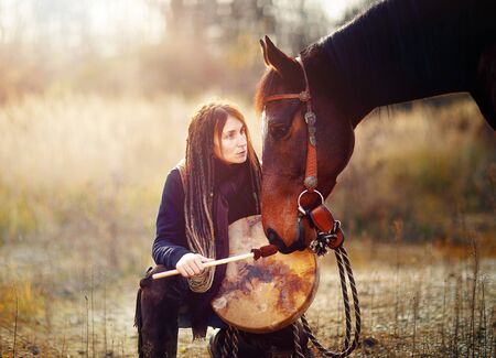 young dreadded girl with her horse and shamanic frame drum.の写真素材