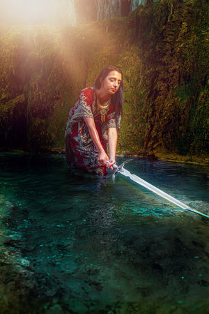 Woman with sword in lake near waterfall.