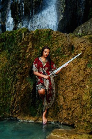 Woman with sword in lake near waterfall.の写真素材