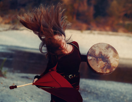 beautiful shamanic girl playing on shaman frame drum in the nature and light graphic effect
