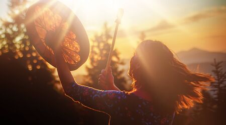 beautiful shamanic girl playing on shaman frame drum in the natureの写真素材