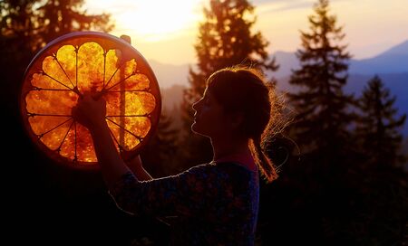 beautiful shamanic girl playing on shaman frame drum in the natureの写真素材