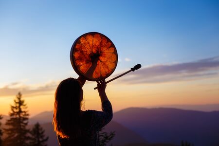 Shamanic girl playing on shaman frame drum in the natureの写真素材