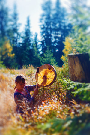 beautiful shamanic girl playing on shaman frame drum in the nature