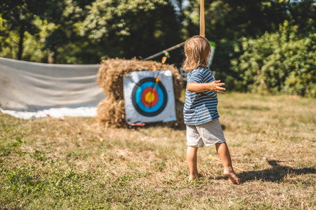 young boy shoots with a wooden bow.