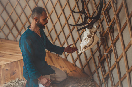 beautiful shamanic man with deer skull in yurt.