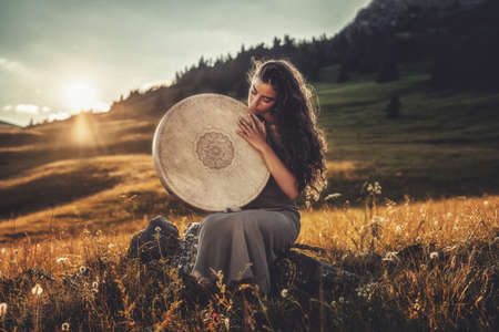 beautiful shamanic girl playing on shaman frame drum in the nature.の写真素材