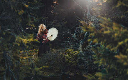 beautiful shamanic girl playing on shaman frame drum in the nature.