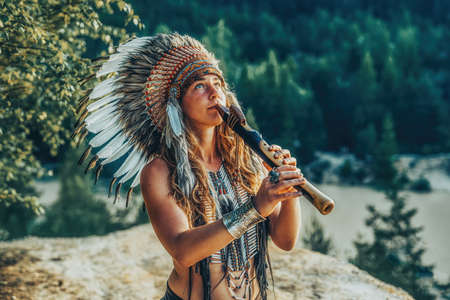 beautiful shamanic girl playing on shaman flute in the nature.の写真素材