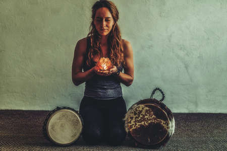 beautiful meditating woman with lotus candle in her hand and djembe.の写真素材