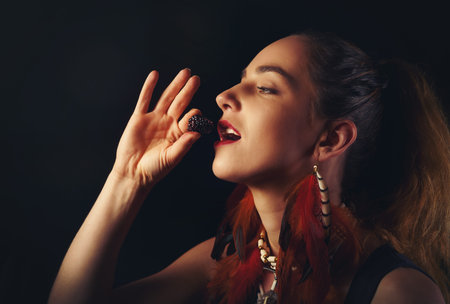 Close up of beautiful woman eating blackberries on black background.