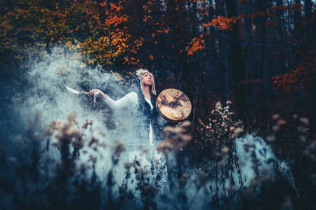 beautiful shamanic girl playing on shaman frame drum in the nature.の写真素材