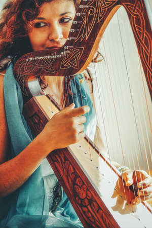 Woman with a harp. Beautiful girl harpist playing her instrument.の写真素材