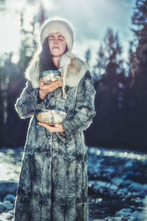 Beautiful shamanic girl playing on tibetian bowl in the nature.の写真素材