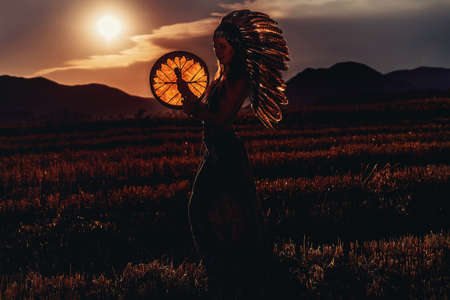 beautiful shamanic girl playing on shaman frame drum in the nature.の写真素材