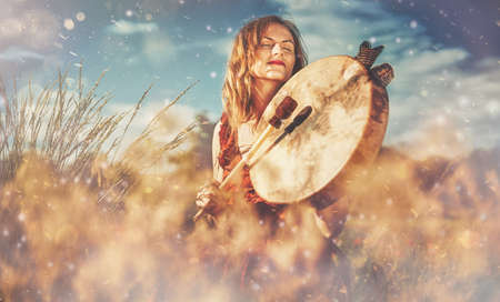 beautiful shamanic girl playing on shaman frame drum in the nature.の写真素材