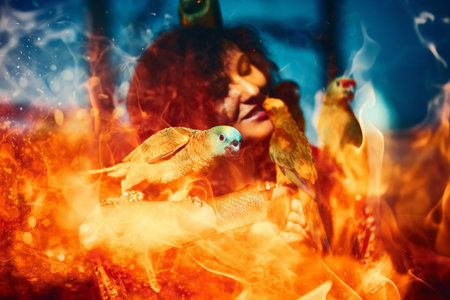 Young woman in ornamental dress and beautiful gold jewelry with a color parrots. fire effect.の写真素材